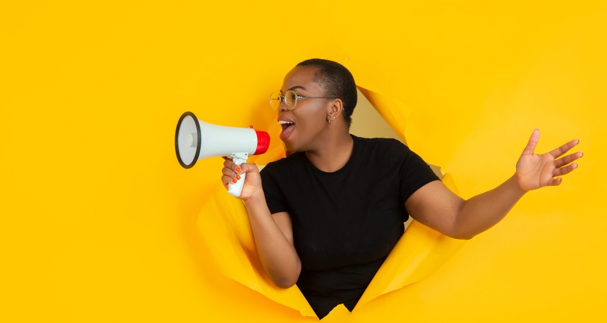 Shouting. Cheerful african-american young woman poses in torn yellow paper background, emotional and expressive. Breaking on, breakthrought. Concept of human emotions, facial expression, sales, ad.